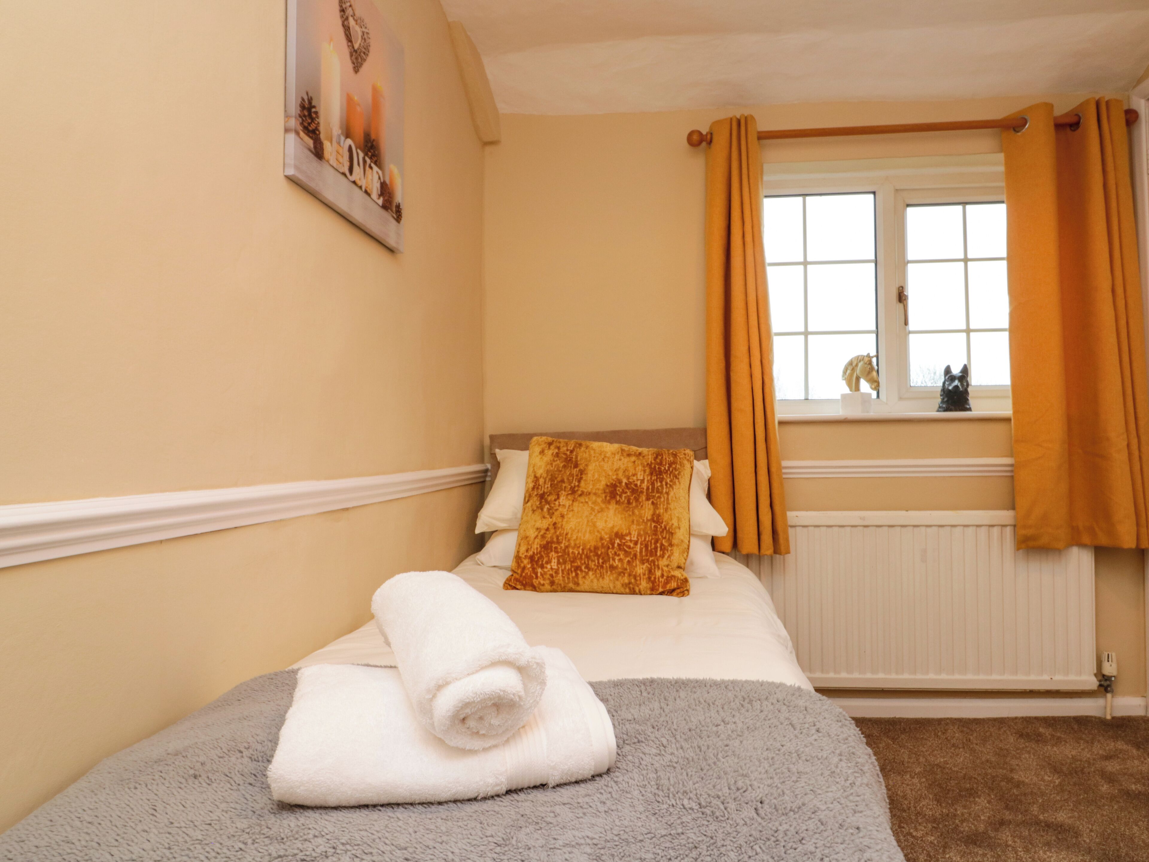 A hotel room with a bed, a window with curtains, a radiator, and a picture on the wall.