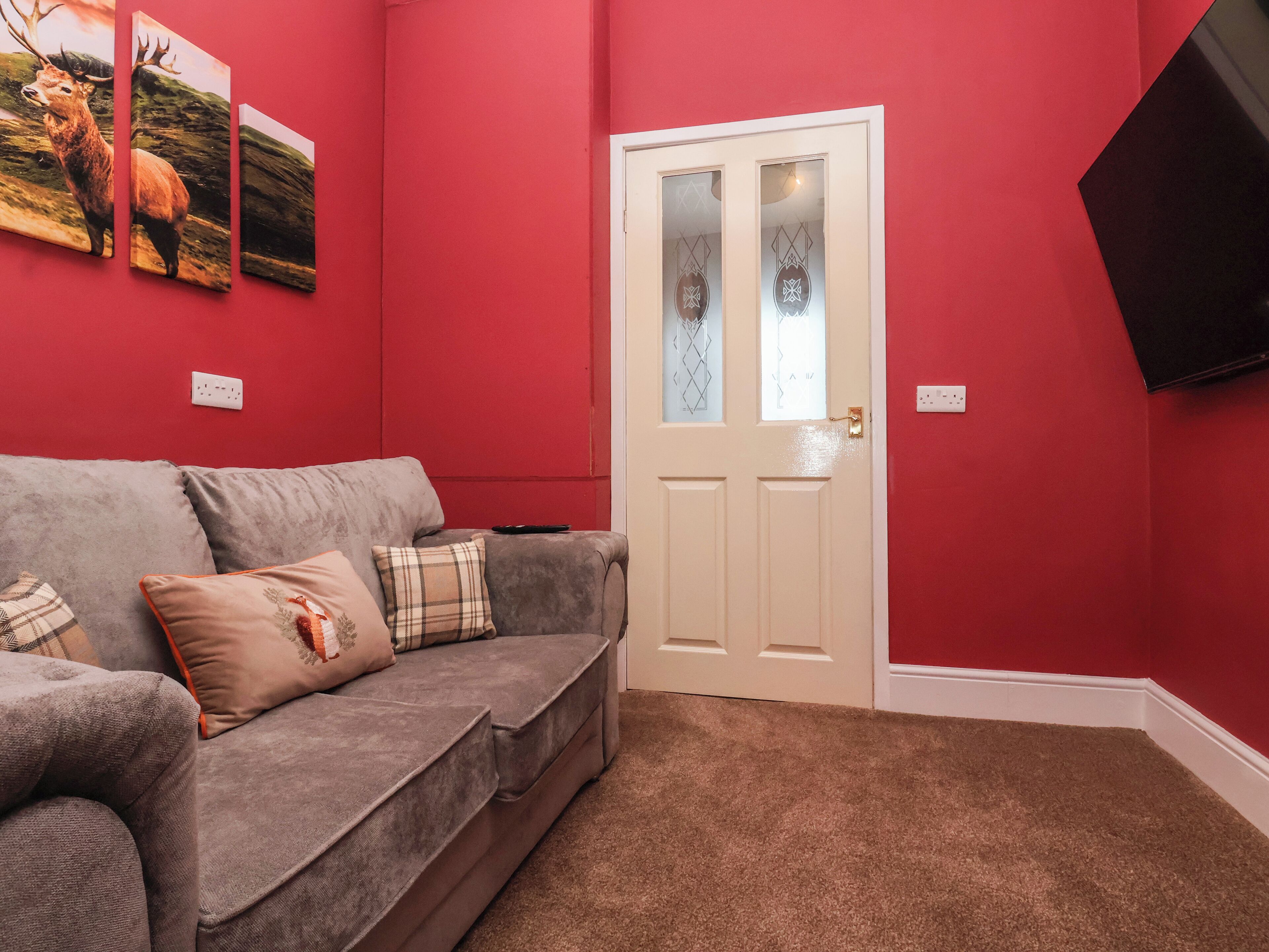 A living room with a grey sofa, a white door, and red walls.