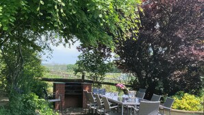 Patio esterno con barbecue in mattoni, circondato da sedie e un tavolo in metallo.