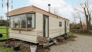 A mobile home with a window, door, and chimney. It has a small porch with steps and a chair. - Upper Calffield Caravan (Haverfordwest)