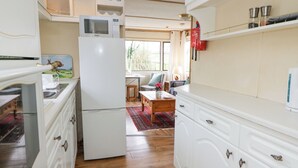 A compact kitchen with white cabinetry, a built-in microwave, and a refrigerator. There is a dining area with a table and chairs, and a window providing natural light. - Upper Calffield Caravan (Haverfordwest)