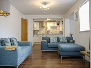 A modern living room with two blue sofas, a wooden door, and a kitchen in the background. - Maceley (Kingsbridge)