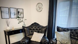 Un salón con un sillón de cuero oscuro, un sofá a juego, una consola de madera y un reloj de pared.