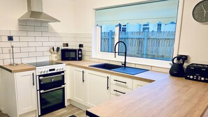 Una cocina compacta con armarios blancos, microondas, hervidor y tostadora.