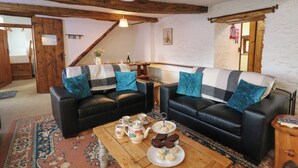 A cozy living room with two black leather sofas, a wooden coffee table with a floral rug, and a dining table set with tea cups and a teapot. - Y Beudy (Llanybydder)