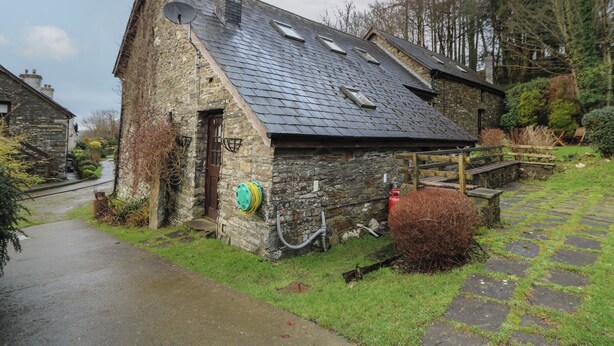 A stone cottage with a sloped roof, a chimney, and a satellite dish. - Y Beudy (Llanybydder)