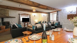 A cozy living room with a fireplace, a sofa set, a dining table set for four, and a television. - Y Beudy (Llanybydder)
