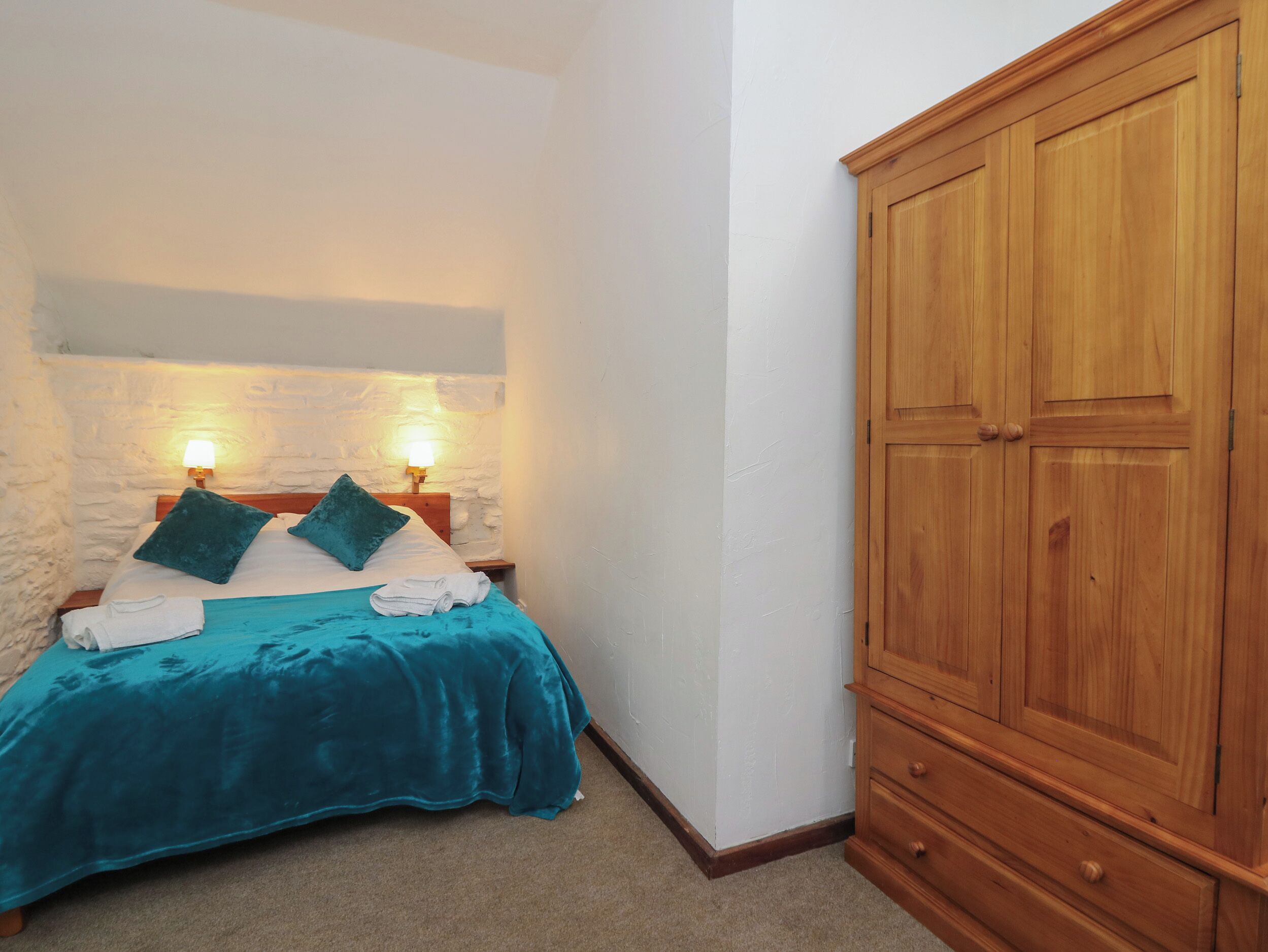 Un dormitorio con cama, dos lámparas de noche, un armario de madera y una pared de piedra.