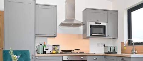 A modern kitchen with grey cabinets, a built-in microwave, a stove, and an oven. There is a dining table with a green placemat and a vase with flowers.
