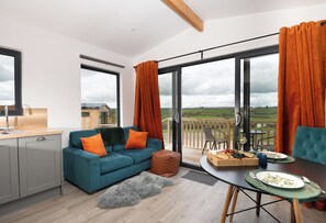 A modern living room with a sofa, dining table, and large windows offering a view of the countryside. - Cae Dafadd (Newtown)