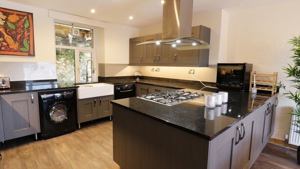 A modern kitchen with a central island, built-in appliances, and a large window. - Old Post Office (Blaenau Ffestiniog)