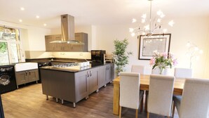 A modern kitchen with a central island, a dining area with a table and chairs, and a hanging light fixture. - Old Post Office (Blaenau Ffestiniog)