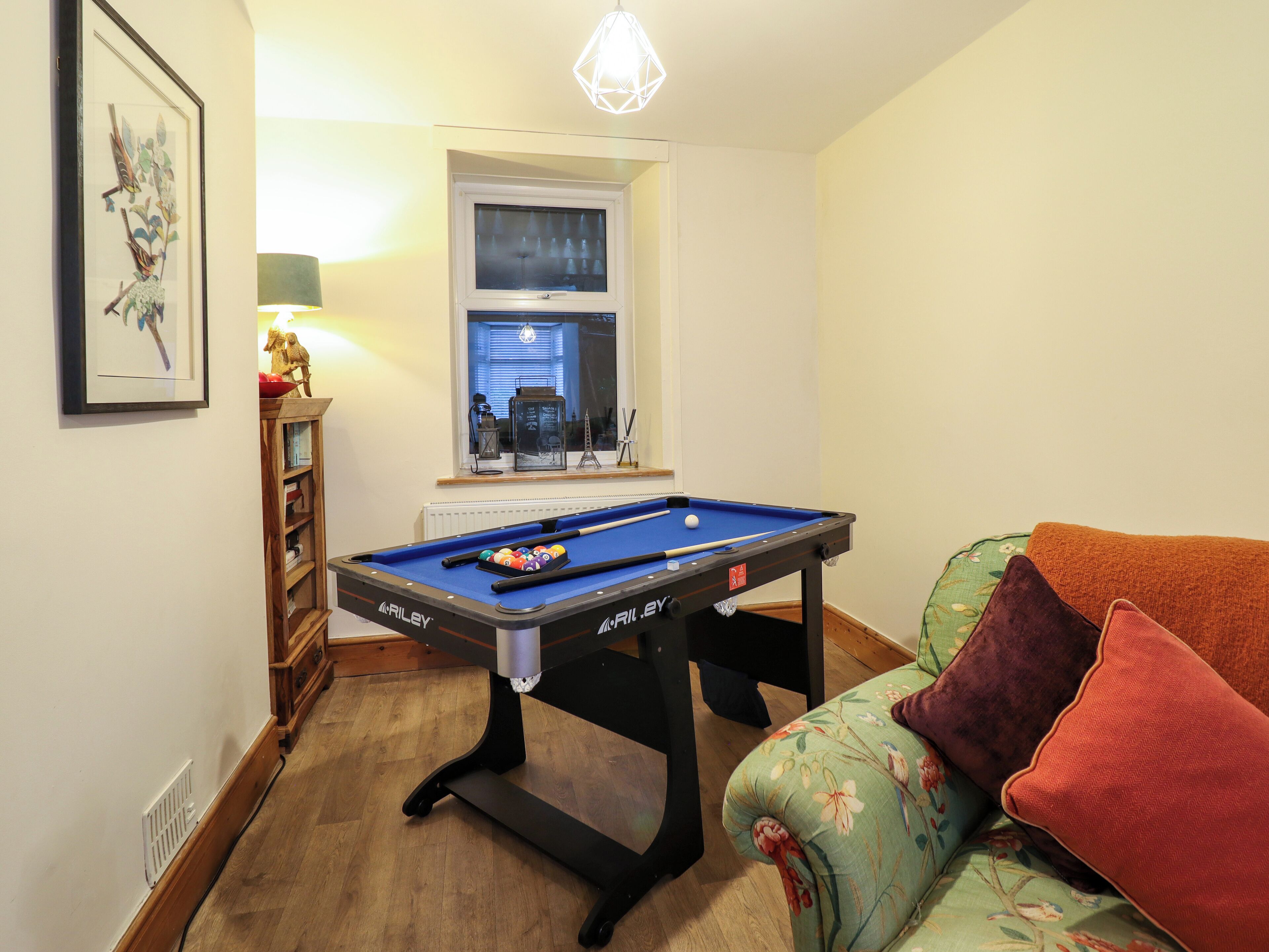 A pool table in a room with a window, a lamp, and a sofa with cushions.