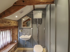A bathroom with a wooden beam ceiling, a white sink, a toilet, and a mirror.