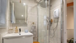 A modern bathroom with a glass shower enclosure, a white vanity with a mirror, and a small stool. - Duck Tavern Annexe (Rhosgoch)