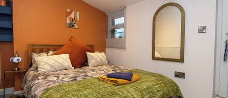 A bedroom with a bed, a nightstand, a lamp, a mirror, and a window with blinds.