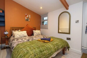 A bedroom with a bed, a nightstand, a lamp, a mirror, and a window with blinds. - Duck Tavern Annexe (Rhosgoch)