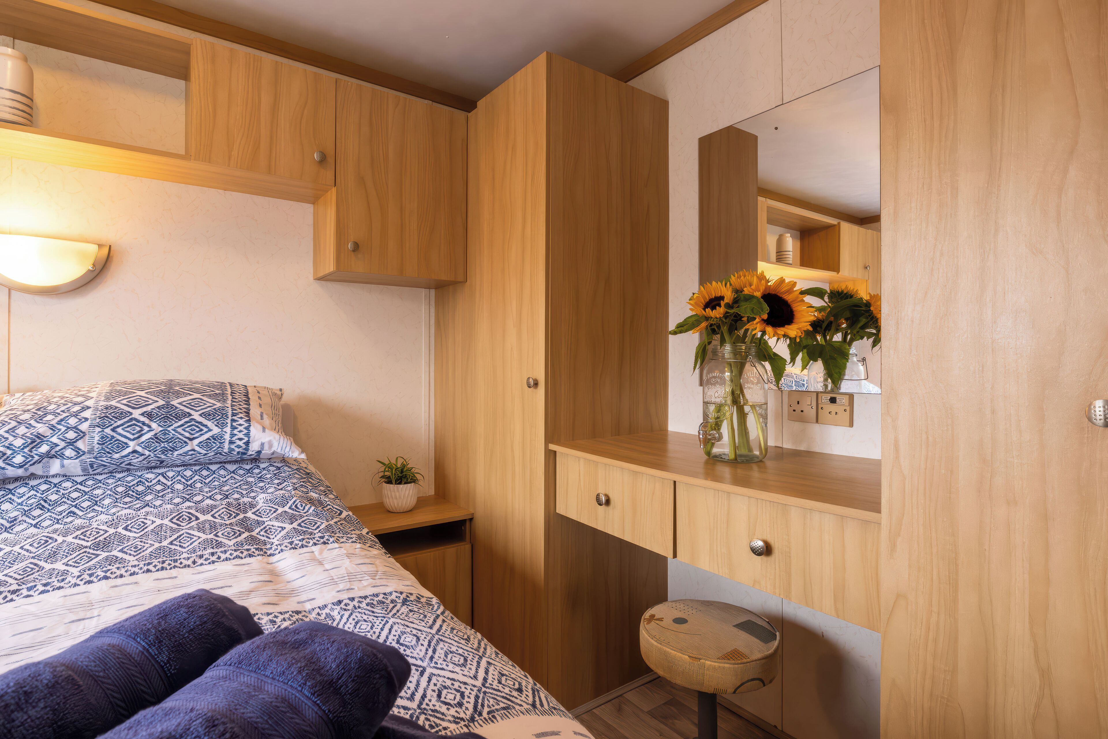 A bedroom with a bed, wooden wardrobe, bedside table, and a mirror.