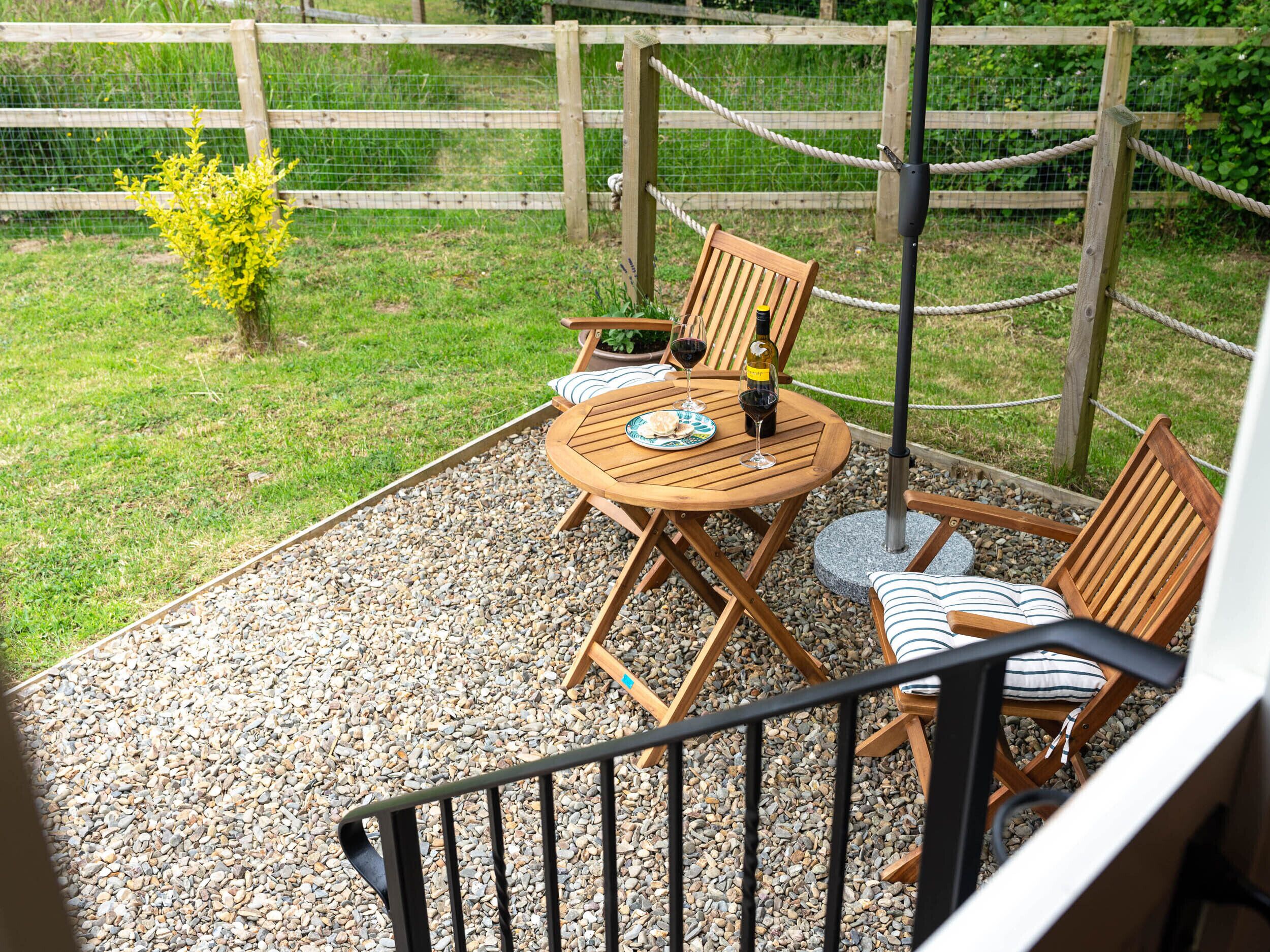 Une terrasse avec une table et des chaises en bois, un petit jardin et une clôture en bois.