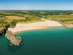 An aerial view of a coastal beach with a sandy shore, clear turquoise waters, and a rocky outcrop on the left. - Bedwen (Llanarth)