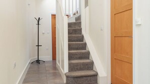 A hallway with a carpeted staircase, wooden doors, and a coat rack. - Beudy Cefn (Porthmadog)