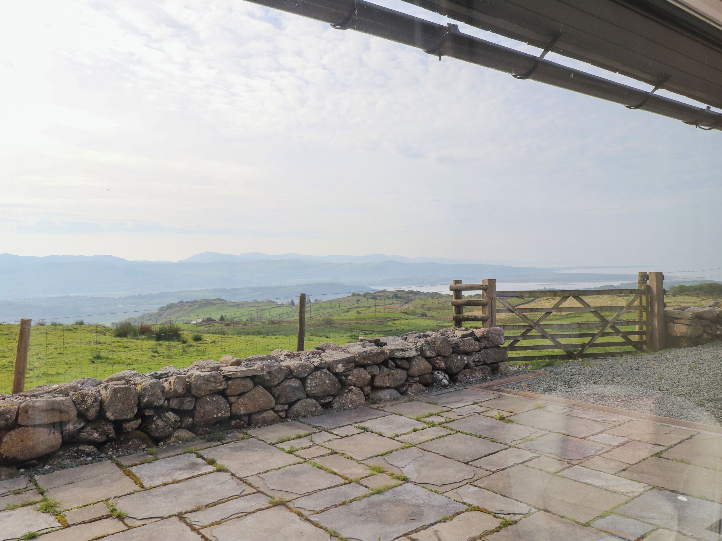 A stone wall and wooden gate leading to a grassy field with distant mountains.