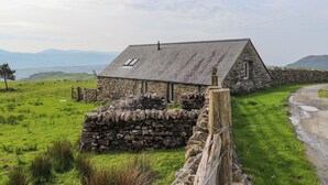 A stone house with a sloped roof, a small window, and a stone wall in a rural setting. - Beudy Cefn (Porthmadog)