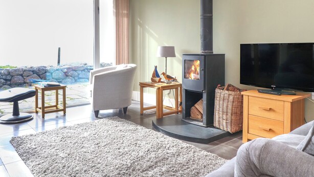 A living room with a fireplace, a television, a sofa, and a view of the outdoors. - Beudy Cefn (Porthmadog)