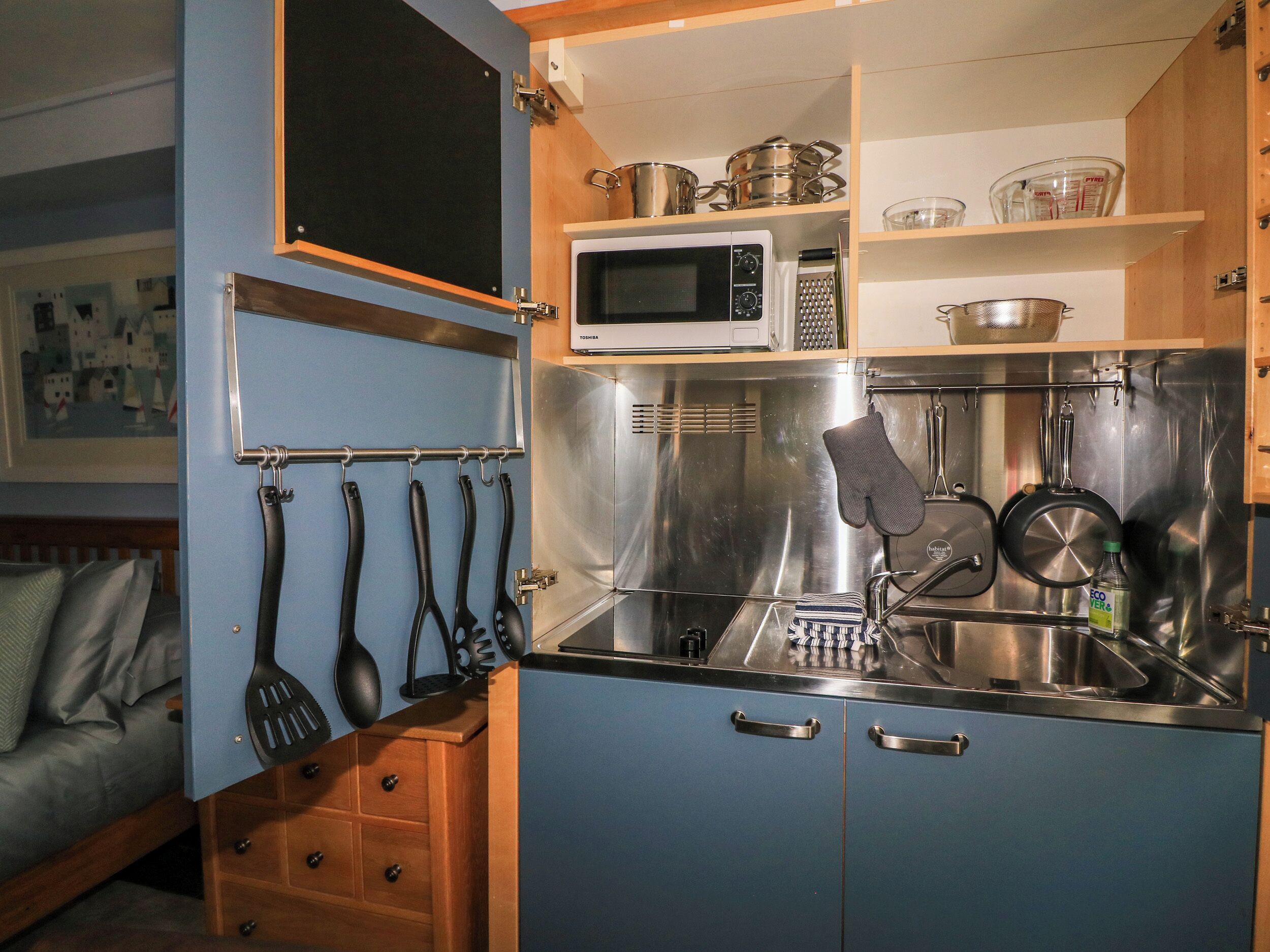 Cocina compacta con microondas, pileta de acero inoxidable y utensilios colgantes.