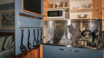 Cocina compacta con microondas, pileta de acero inoxidable y utensilios colgantes.