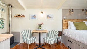 A cozy room with a bed, a table with chairs, a shelf with jars, and two framed pictures on the wall. - Collen (Llanarth)