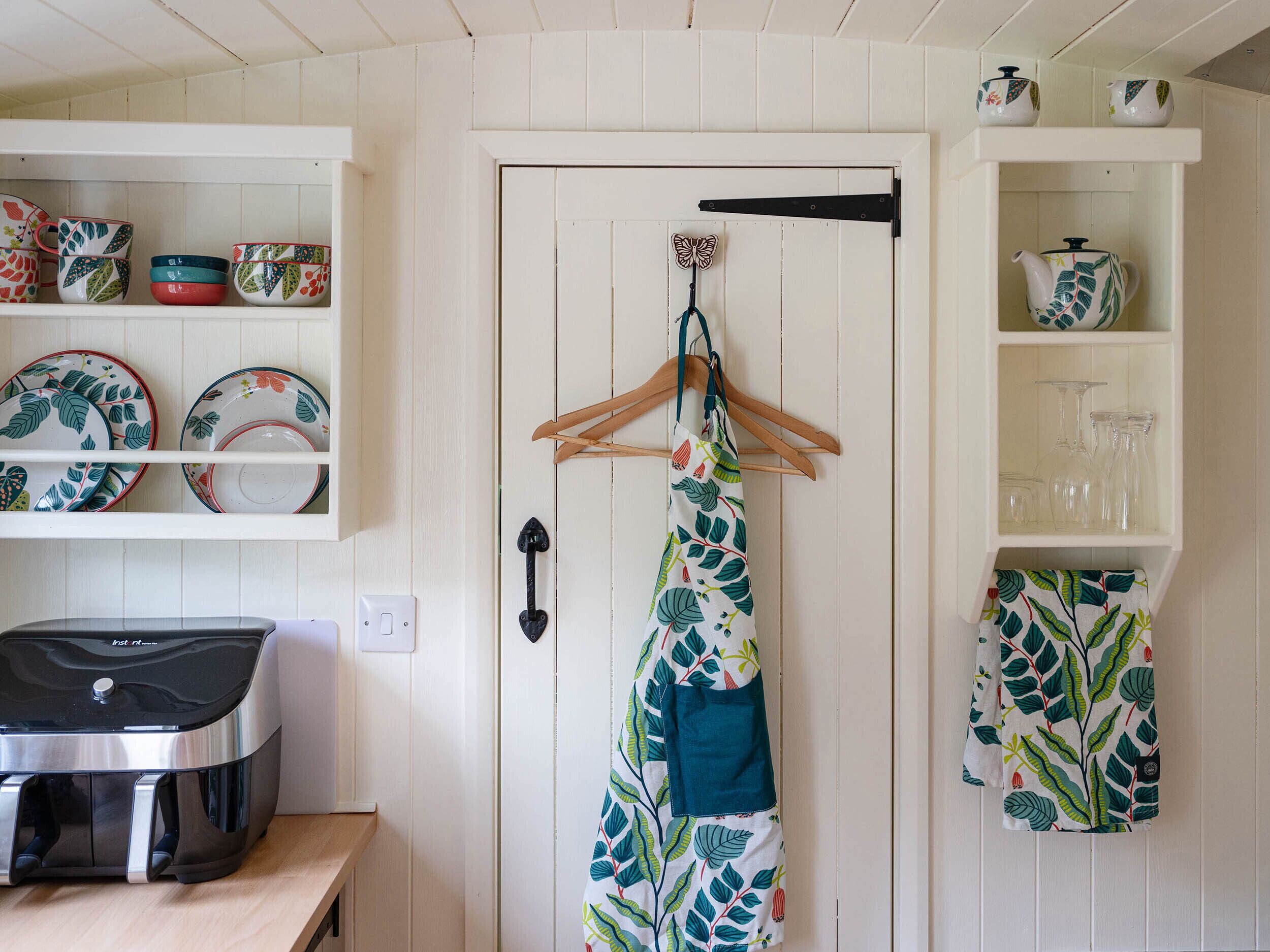 A kitchen with white wooden cabinets, a hanging apron, and a coffee maker on the counter.