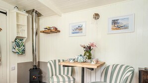 A cozy room with a wood-burning stove, striped chairs, a small table with a vase of flowers, and two framed pictures on the wall. - Collen (Llanarth)
