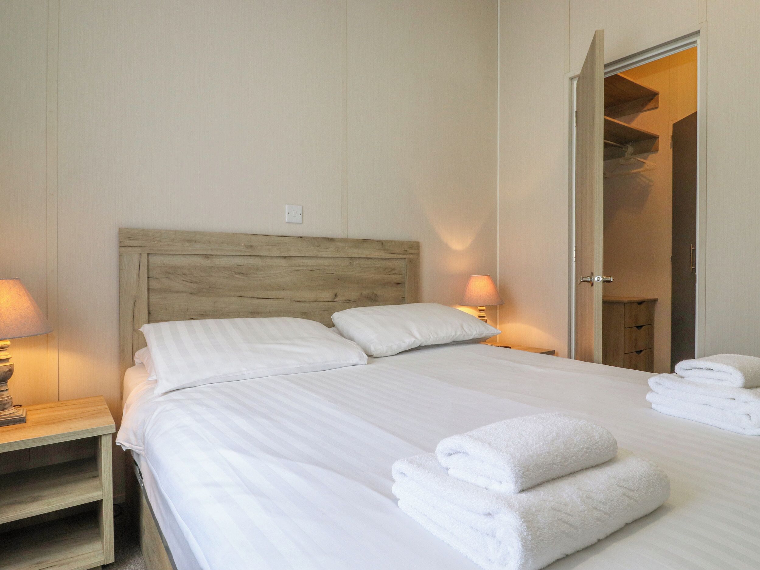 A neatly made bed with white linens and pillows, two bedside lamps, and a wooden headboard.