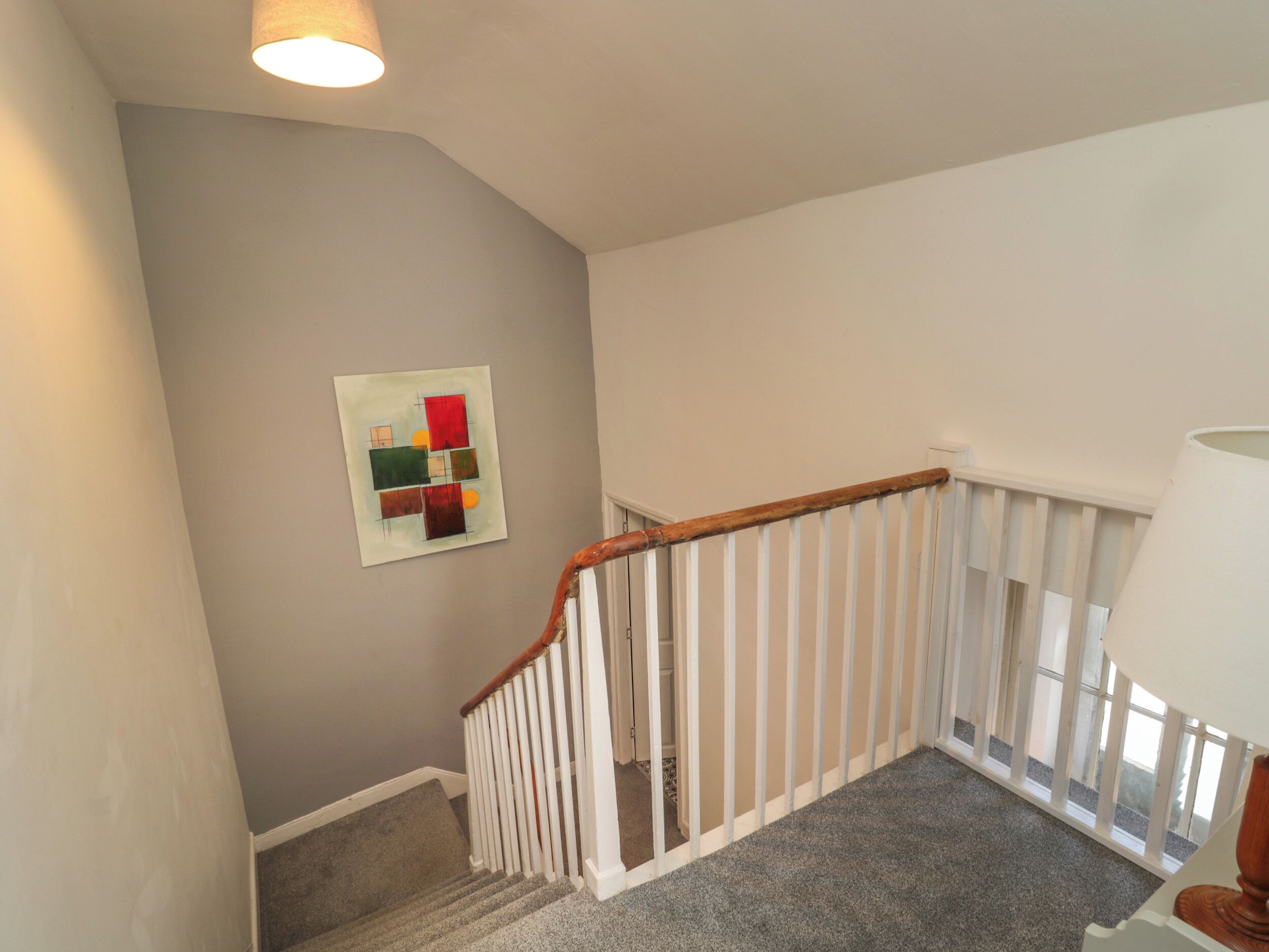 Un escalier avec une rampe en bois et des balustrades blanches, des marches recouvertes de moquette et une œuvre d’art abstraite accrochée au mur.