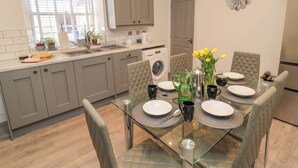 A modern kitchen with grey cabinets, a glass dining table, and a view of the outside through a window. - The Old Factory House (Berwick-upon-Tweed)
