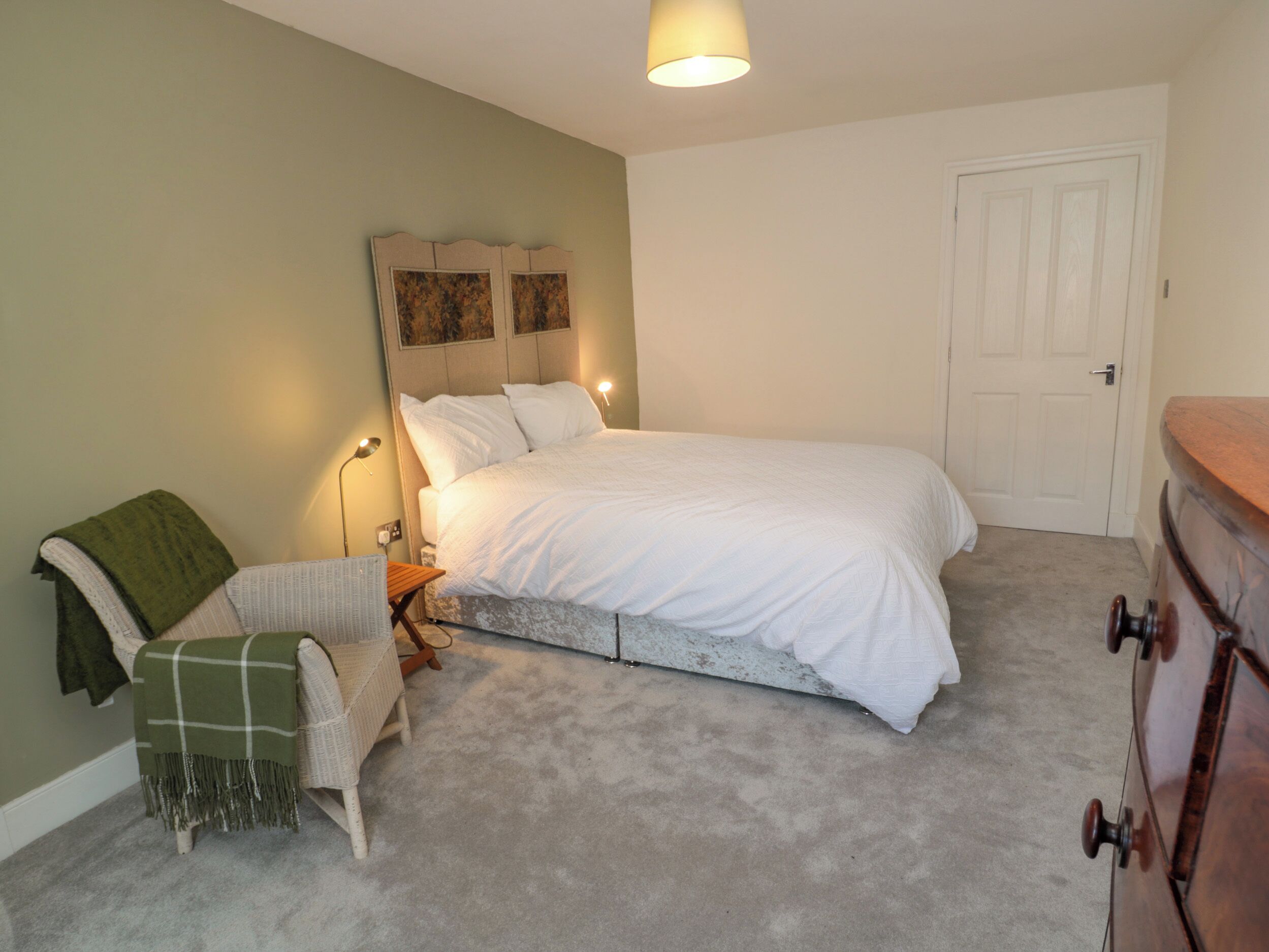 Une chambre à coucher comprenant un lit, une table de chevet, une lampe, une chaise et une commode.