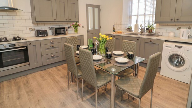 A modern kitchen with grey cabinets, a microwave, a stove, and a washing machine. - The Old Factory House (Berwick-upon-Tweed)