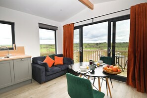 A modern living room with a sofa, a dining table with breakfast items, and large windows with curtains. - Cae Bedw (Newtown)