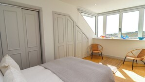 A bedroom with a bed, two doors, a window with a view, and a chair. - Ocean View (Alnwick)