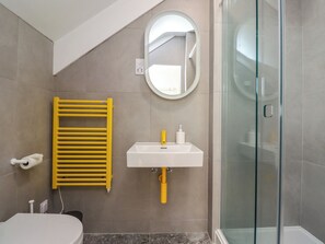 A bathroom with a toilet, a sink with a mirror, a glass shower enclosure, and a yellow towel rack. - Ocean View (Alnwick)