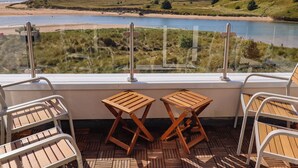 A balcony with two wooden tables and chairs, overlooking a beach and grassy landscape. - Ocean View (Alnwick)