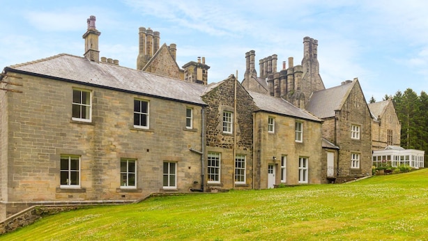 A row of stone buildings with multiple chimneys, a grassy lawn, and a clear sky. - The Coach House (Belford)