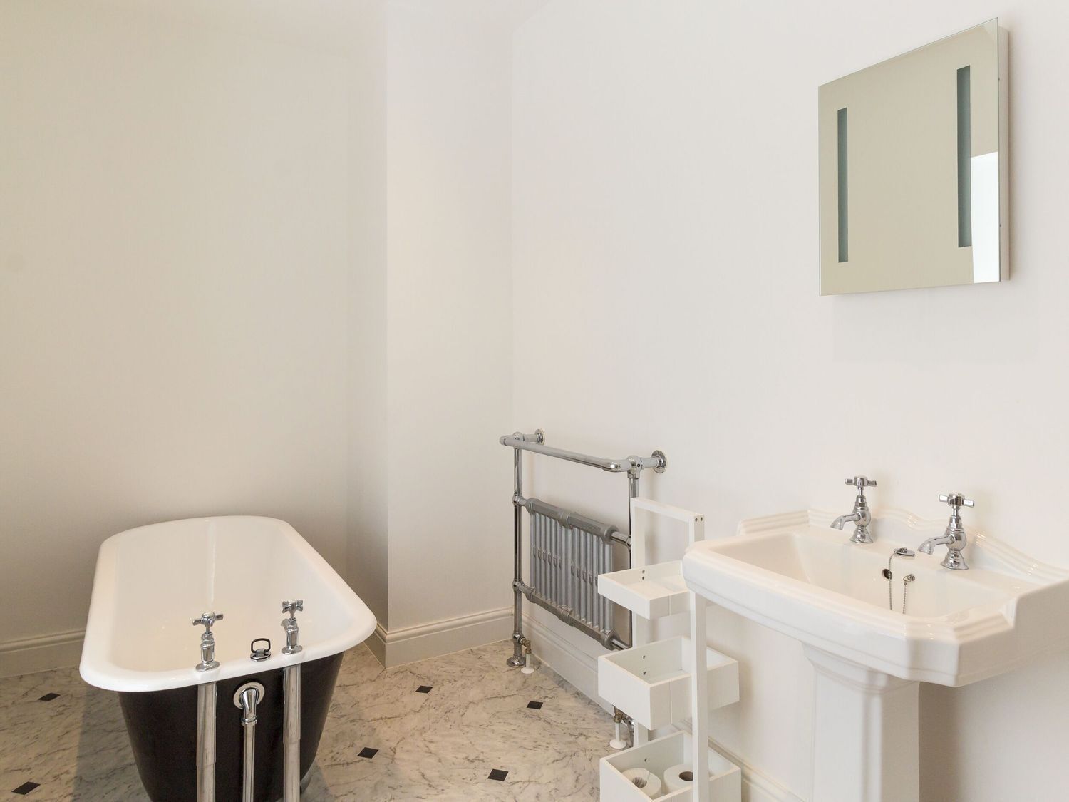 Un baño con una bañera independiente, un radiador y un lavabo doble con un espejo arriba.
