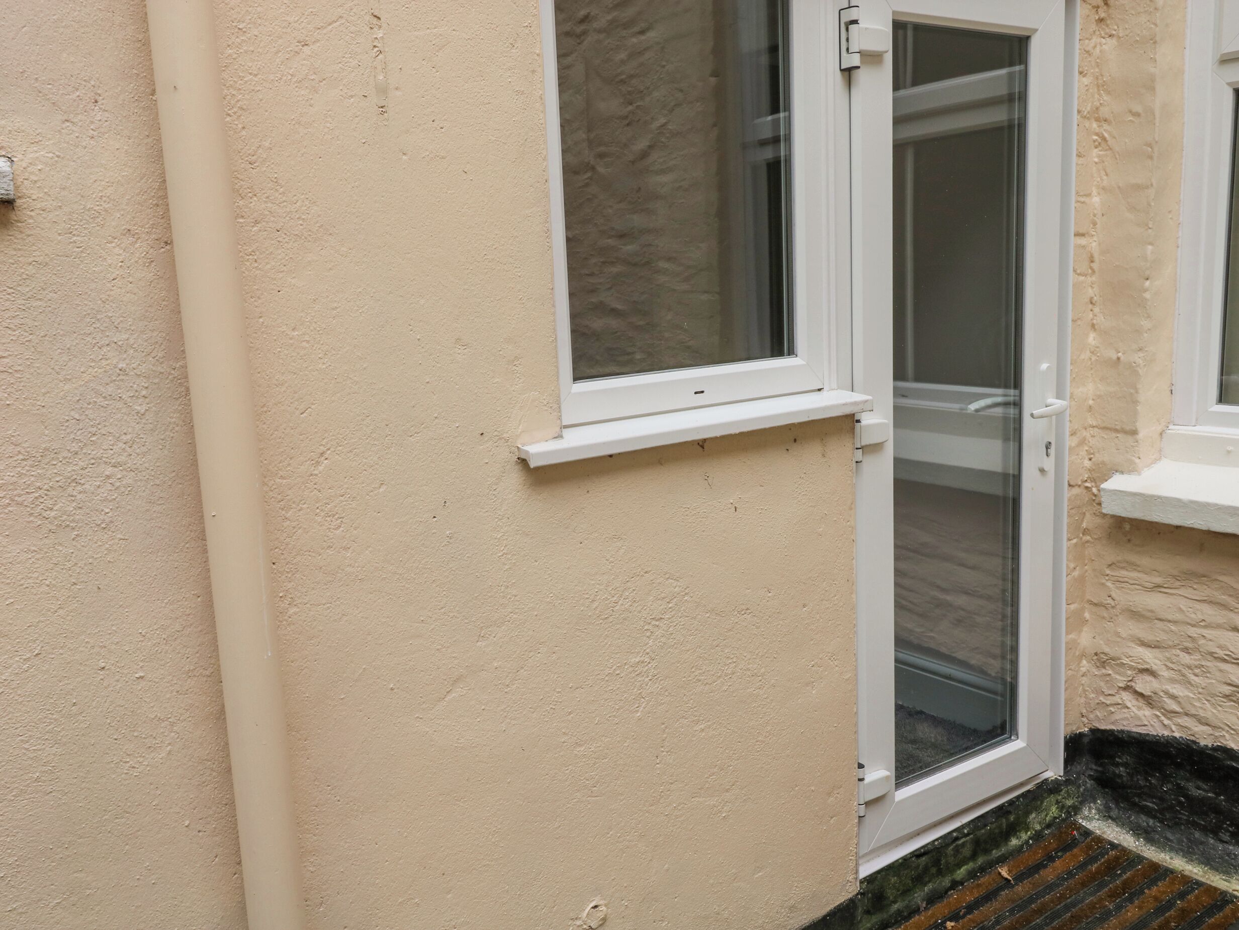 A white-framed door with a glass panel, beige textured wall, and a small white window above it.