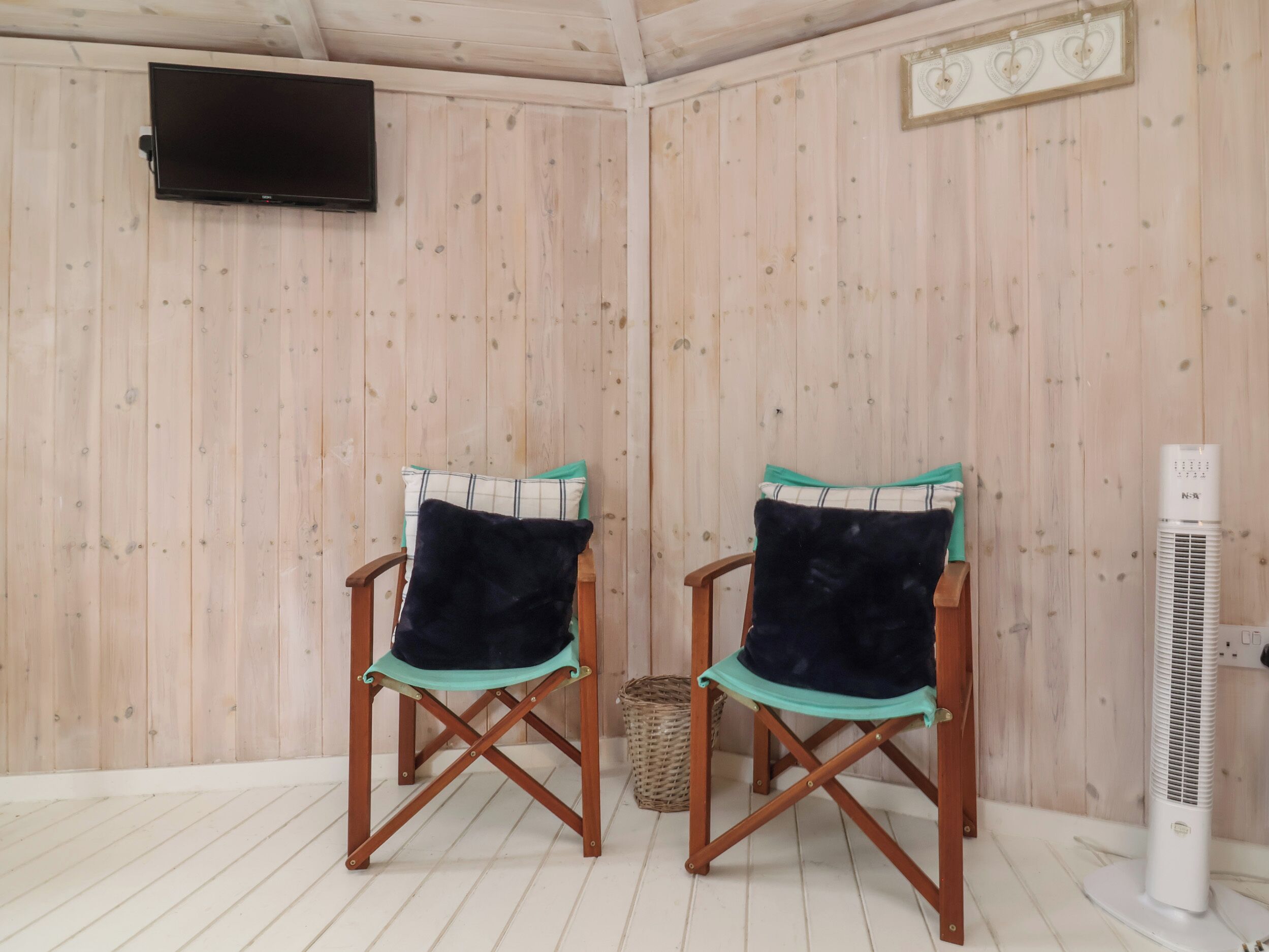 Une pièce comprenant deux chaises pliantes en bois avec des coussins de couleur turquoise, un téléviseur fixé au mur et un climatiseur sur pied.