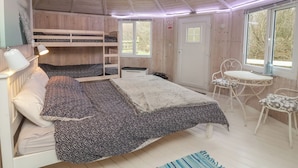 Une pièce confortable avec un lit superposé, un bureau et une chaise. Il y a une fenêtre donnant sur les arbres et une porte avec une pancarte.