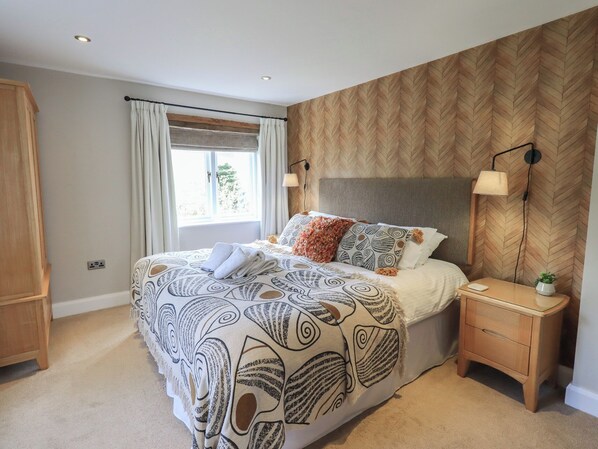 A bedroom with a bed, bedside tables, a window with curtains, and a herringbone-patterned wall. - Haystacks (Windermere)