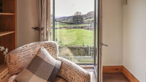 A cozy room with a large window, a wooden bookshelf, and a patterned sofa. - Haystacks (Windermere)