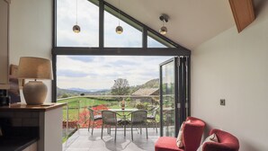 A modern kitchen with a large window, a dining area with a table and chairs, and a red upholstered chair. - Haystacks (Windermere)